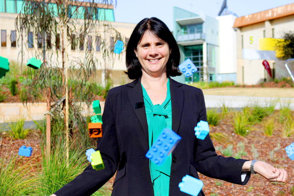 Dr Kim Simoncini stands on the UC Concourse with colourful Duplo blocks raining around her