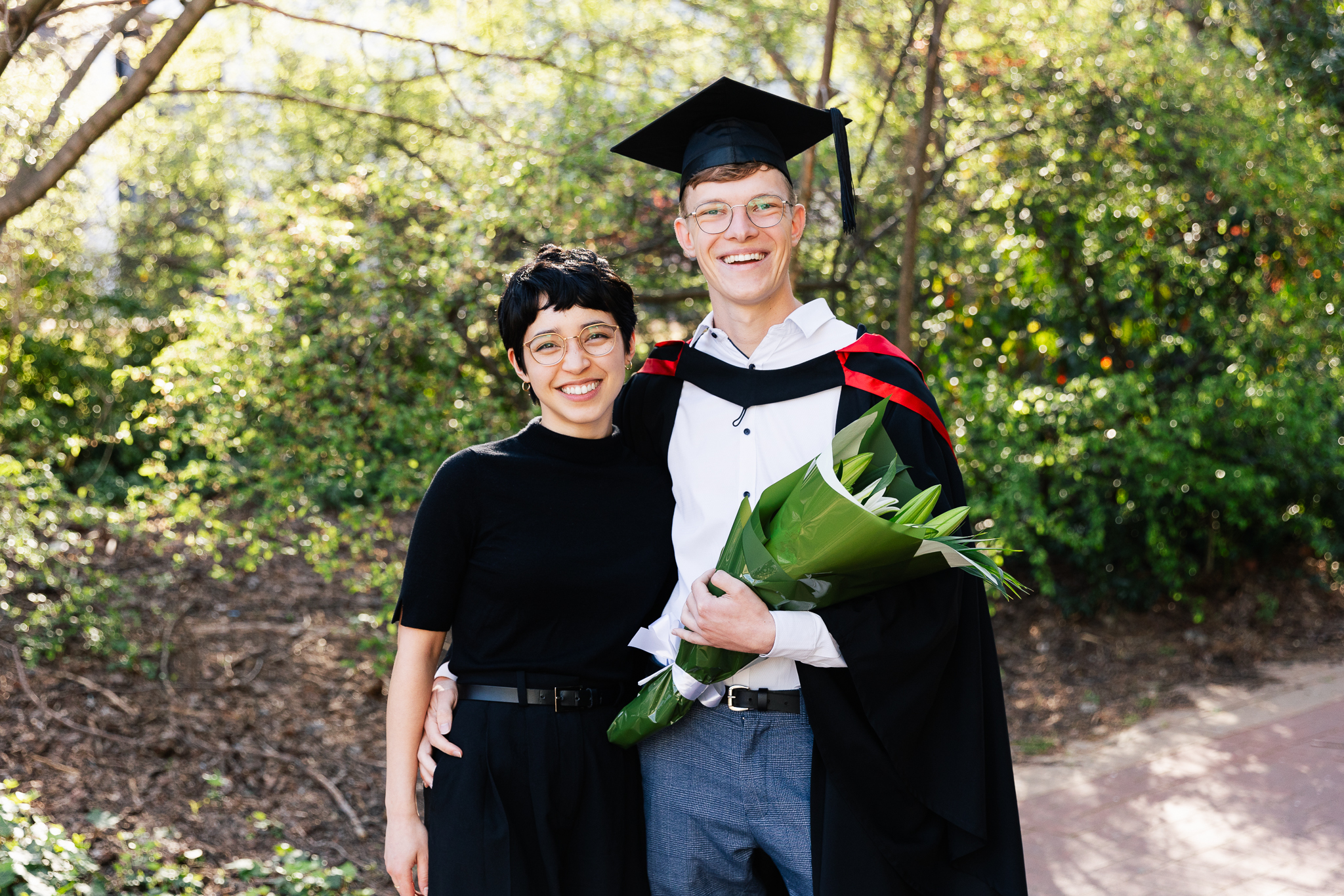 A man in a graduation cap holds flowers and poses with a woman 