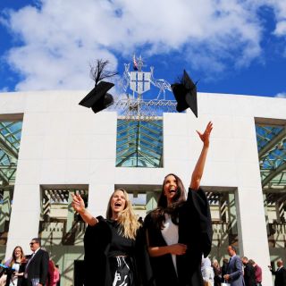 Two graduates throw their mortarboards in the air as they celebrate graduating from the University of Canberra