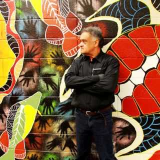 Paul Collis standing in front of Aboriginal artwork